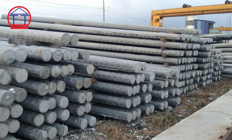 Cột điện bê tông ly tâm: phân nhóm, ký hiệu và cách chọn Bãi thành phẩm cột điện bê tông ly tâm xếp thành nhiều lớp tại nhà máy, phía sau là cầu trục và khu vực sản xuất