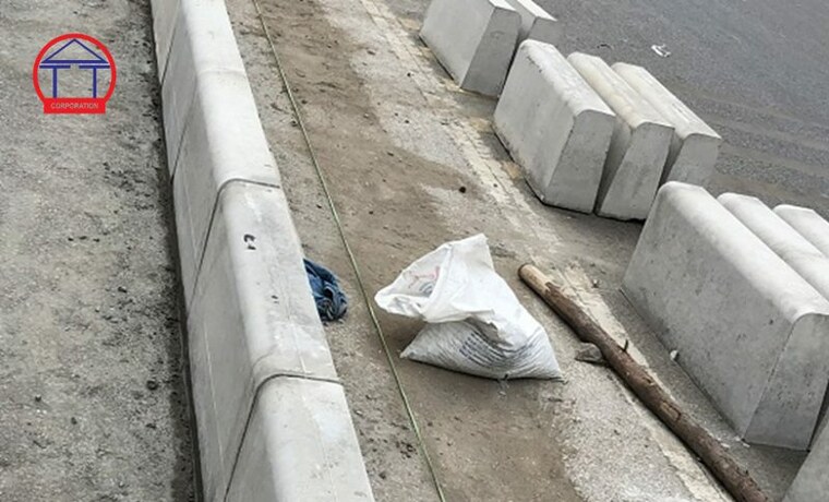 Bó vỉa bê tông giả đá: cách tạo vân, tiêu chuẩn, nghiệm thu Tuyến bó vỉa bê tông đúc sẵn đang lắp đặt dọc mép đường tại công trình, các viên chờ lắp xếp bên cạnh