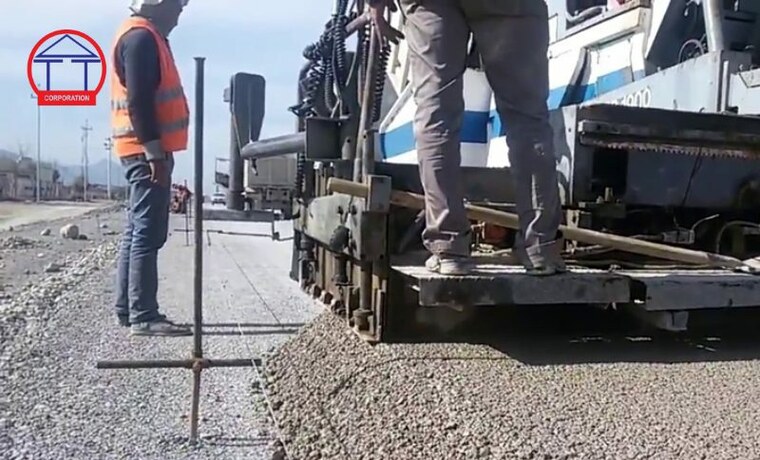 Cấp phối đá dăm gia cố xi măng: tiêu chuẩn TCVN 8858:2023 Máy rải đang rải lớp cấp phối đá dăm, công nhân dùng thước kiểm tra chiều dày lớp rải tại công trường làm đường
